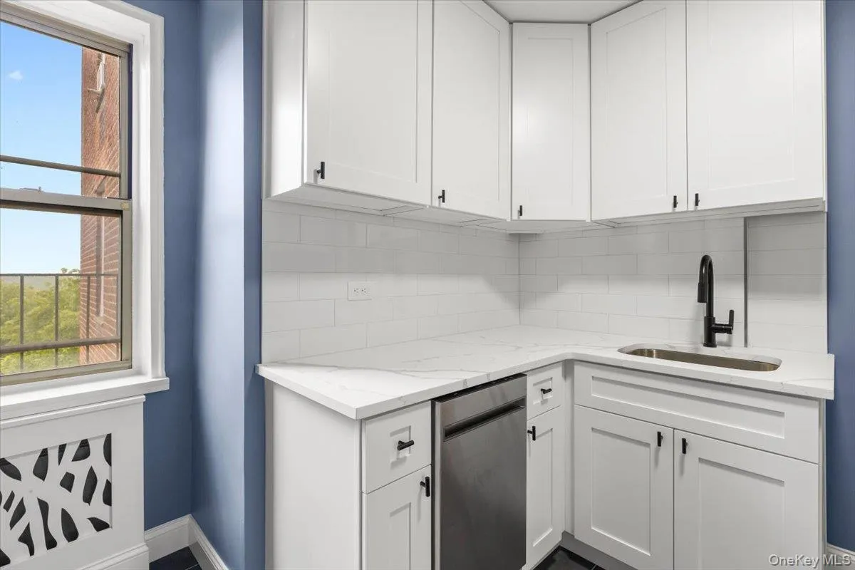 Modern kitchen area featuring white shaker-style cabinetry, a white subway tile backsplash, and light-toned countertops Modern kitchen area featuring white shaker-style cabinetry, a white subway tile backsplash, and light-toned countertops