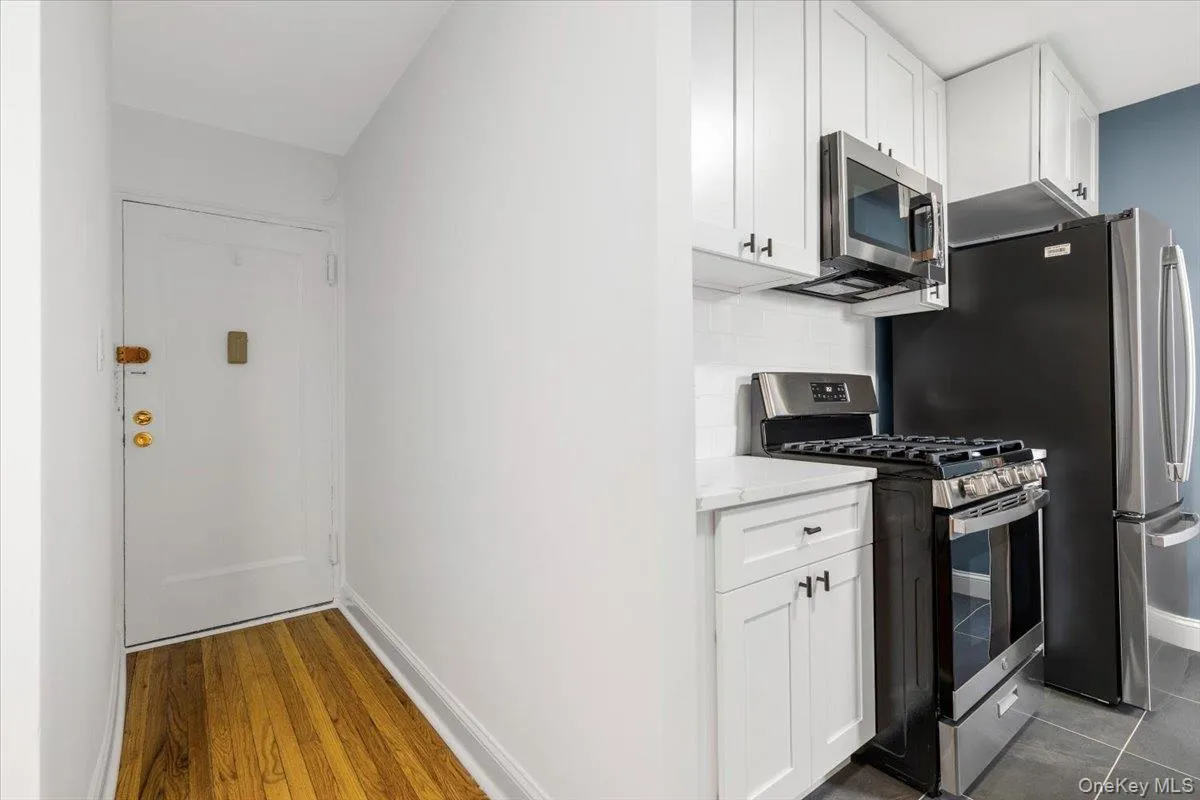 Compact kitchen featuring white shaker cabinetry, stainless steel appliances, a white subway tile backsplash, and light-colored countertops Compact kitchen featuring white shaker cabinetry, stainless steel appliances, a white subway tile backsplash, and light-colored countertops