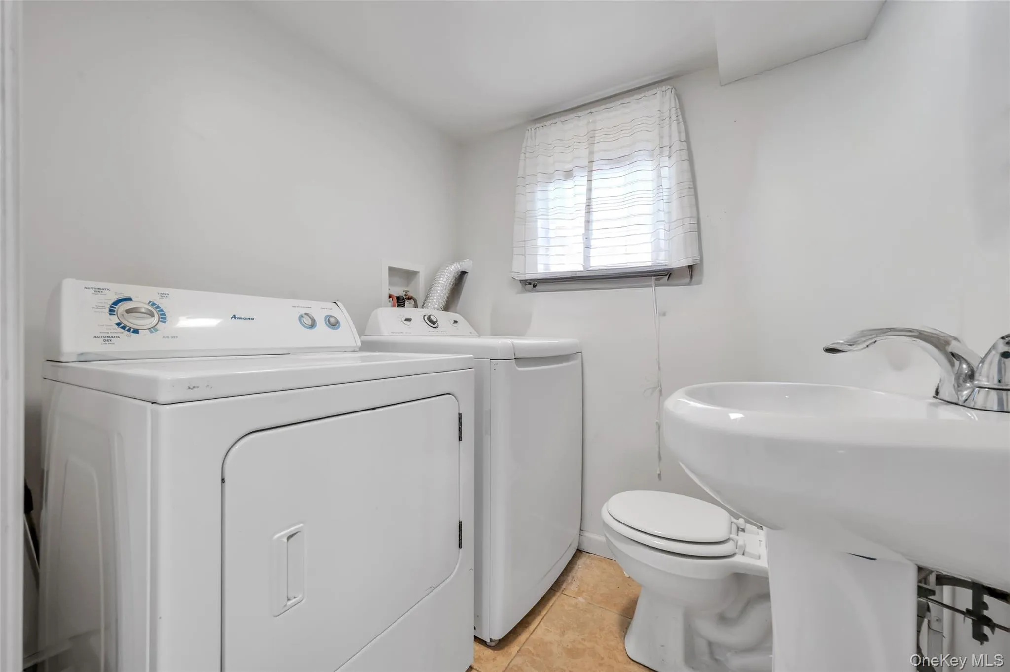 Dedicated laundry area featuring a white front-loading dryer, a white top-loading washing machine, a pedestal sink with chrome faucet, and a toilet Dedicated laundry area featuring a white front-loading dryer, a white top-loading washing machine, a pedestal sink with chrome faucet, and a toilet