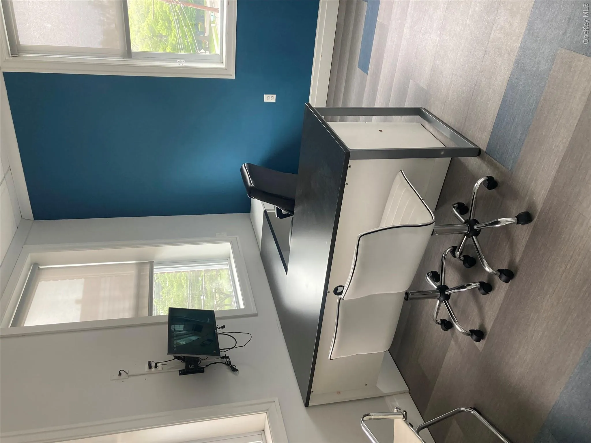 Room featuring three windows with roller blinds, a distinct blue accent wall, and wood-finish flooring with patterned blue accents Room featuring three windows with roller blinds, a distinct blue accent wall, and wood-finish flooring with patterned blue accents