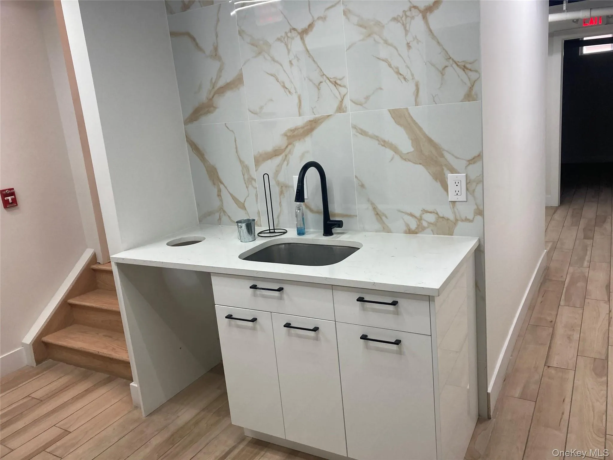 Modern kitchenette featuring a stainless steel sink, matte black faucet, white cabinetry with black hardware, and a light-toned countertop Modern kitchenette featuring a stainless steel sink, matte black faucet, white cabinetry with black hardware, and a light-toned countertop