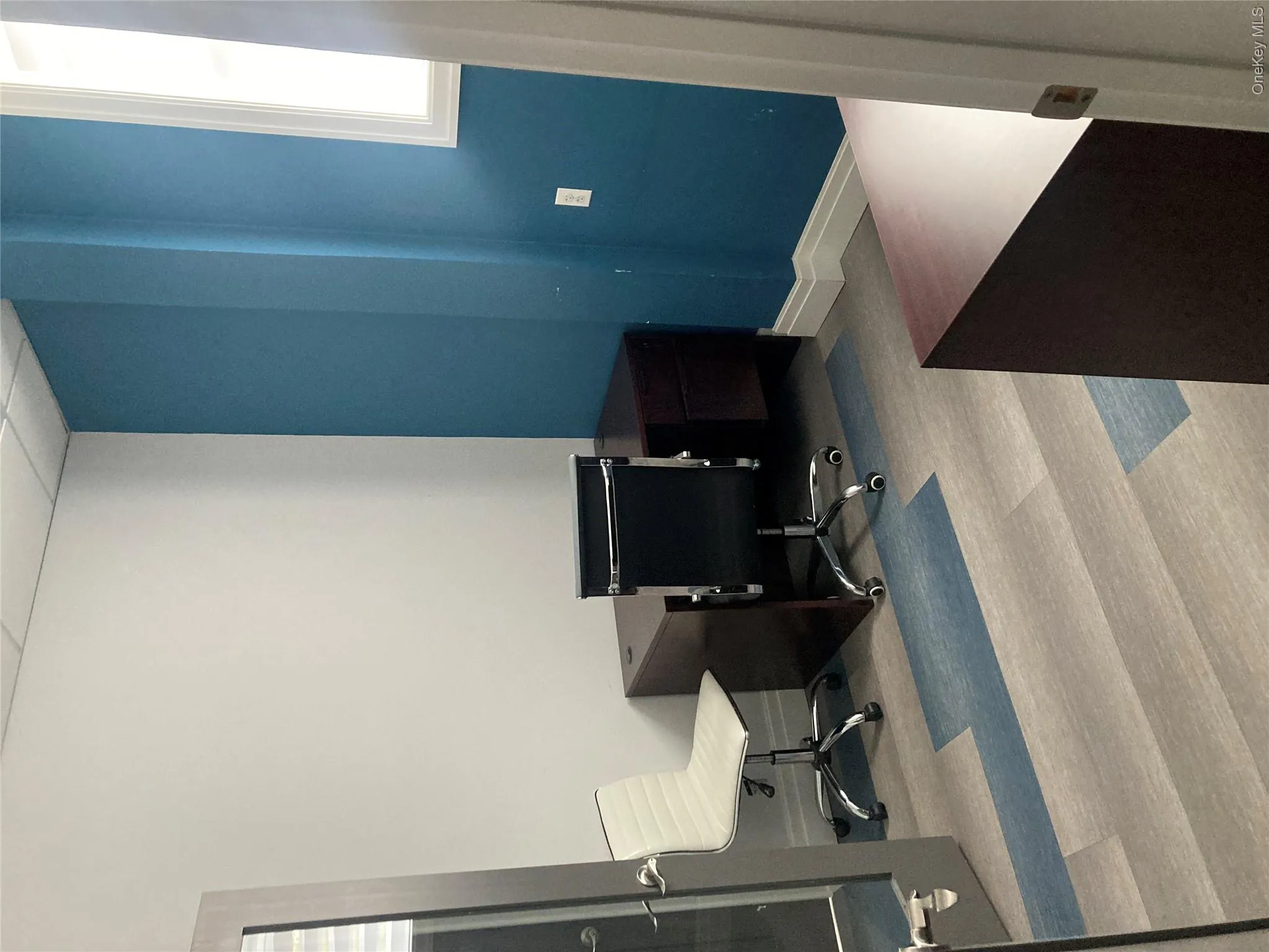 Office space featuring a window, wood-finish flooring with blue accents, white walls, and a prominent blue accent wall Office space featuring a window, wood-finish flooring with blue accents, white walls, and a prominent blue accent wall