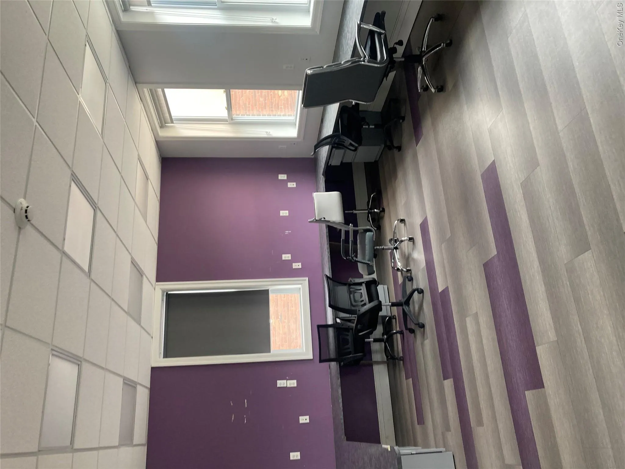 Spacious room featuring purple accent walls, light wood-finish flooring with purple accents, and multiple windows with roller shades Spacious room featuring purple accent walls, light wood-finish flooring with purple accents, and multiple windows with roller shades