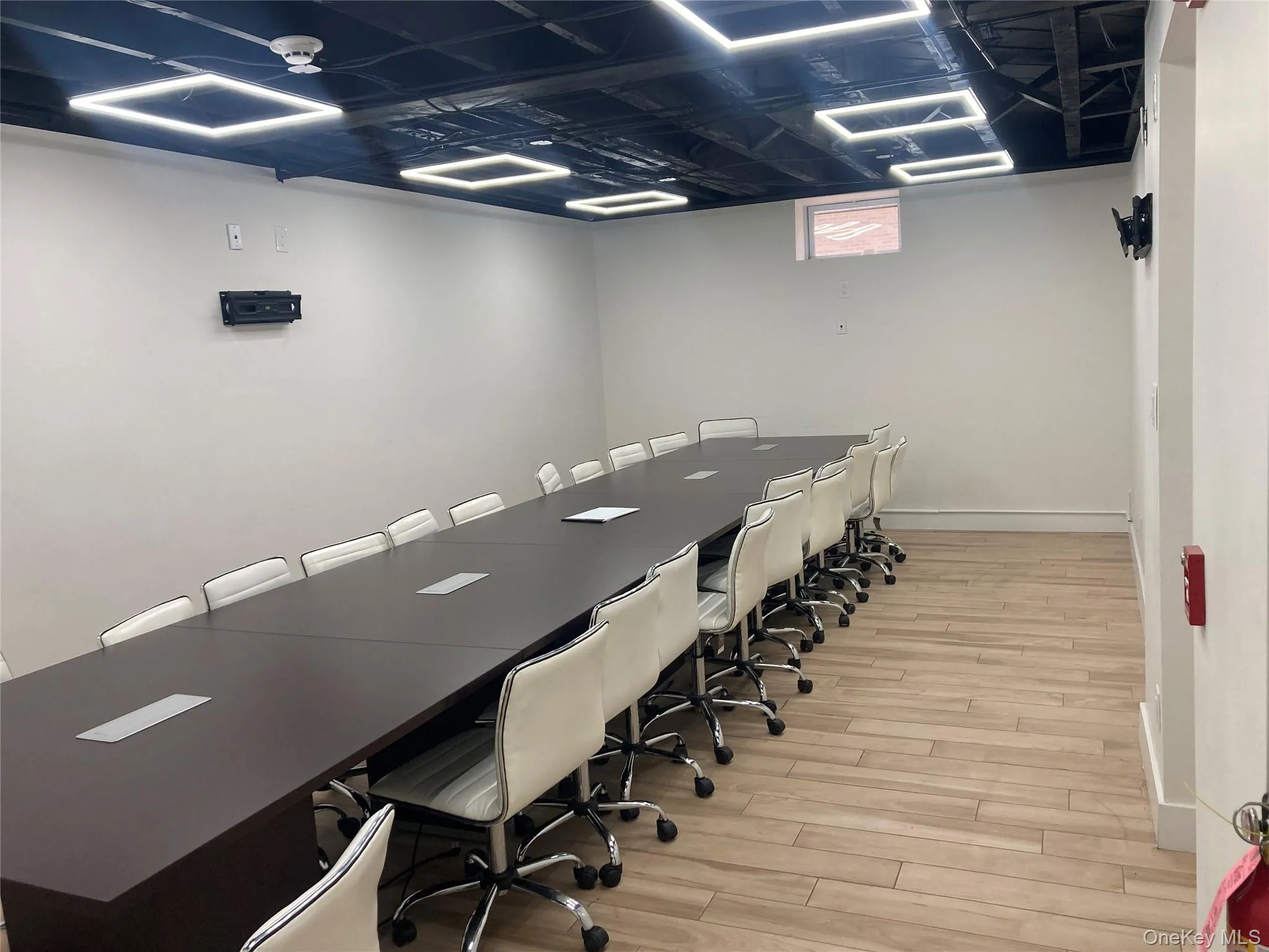 Spacious room featuring a long conference table with integrated power outlets, wood-finish flooring, and bright overhead lighting Spacious room featuring a long conference table with integrated power outlets, wood-finish flooring, and bright overhead lighting