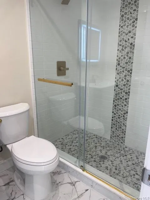 Bathroom featuring marble look tiles, toilet, and a stall shower Bathroom featuring marble look tiles, toilet, and a stall shower