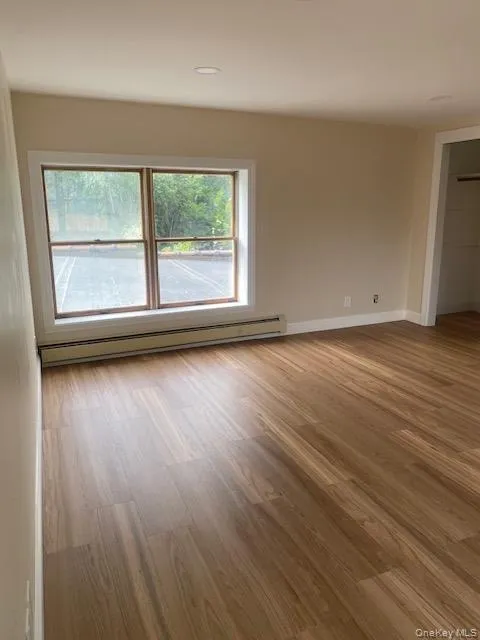 Unfurnished room featuring baseboard heating, wood finished floors, and baseboards Unfurnished room featuring baseboard heating, wood finished floors, and baseboards