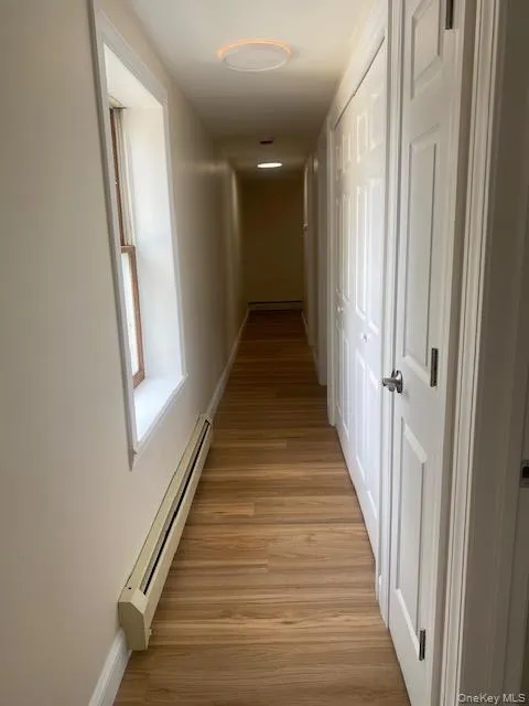 Corridor featuring a baseboard radiator, baseboards, and light wood finished floors Corridor featuring a baseboard radiator, baseboards, and light wood finished floors