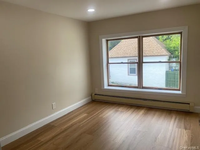 Empty room with baseboard heating, healthy amount of natural light, wood finished floors, baseboards, and recessed lighting Empty room with baseboard heating, healthy amount of natural light, wood finished floors, baseboards, and recessed lighting