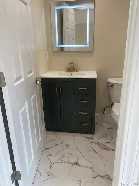 Half bathroom with marble look tile flooring, vanity, toilet, and baseboards Half bathroom with marble look tile flooring, vanity, toilet, and baseboards