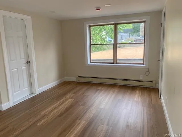 Empty room featuring baseboard heating, wood finished floors, and baseboards Empty room featuring baseboard heating, wood finished floors, and baseboards