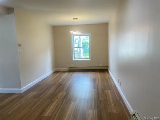 Spare room with baseboard heating, wood finished floors, and baseboards Spare room with baseboard heating, wood finished floors, and baseboards