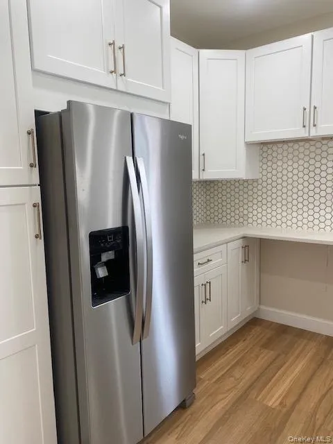 Kitchen with stainless steel fridge, white cabinetry, light countertops, and light wood-style floors Kitchen with stainless steel fridge, white cabinetry, light countertops, and light wood-style floors