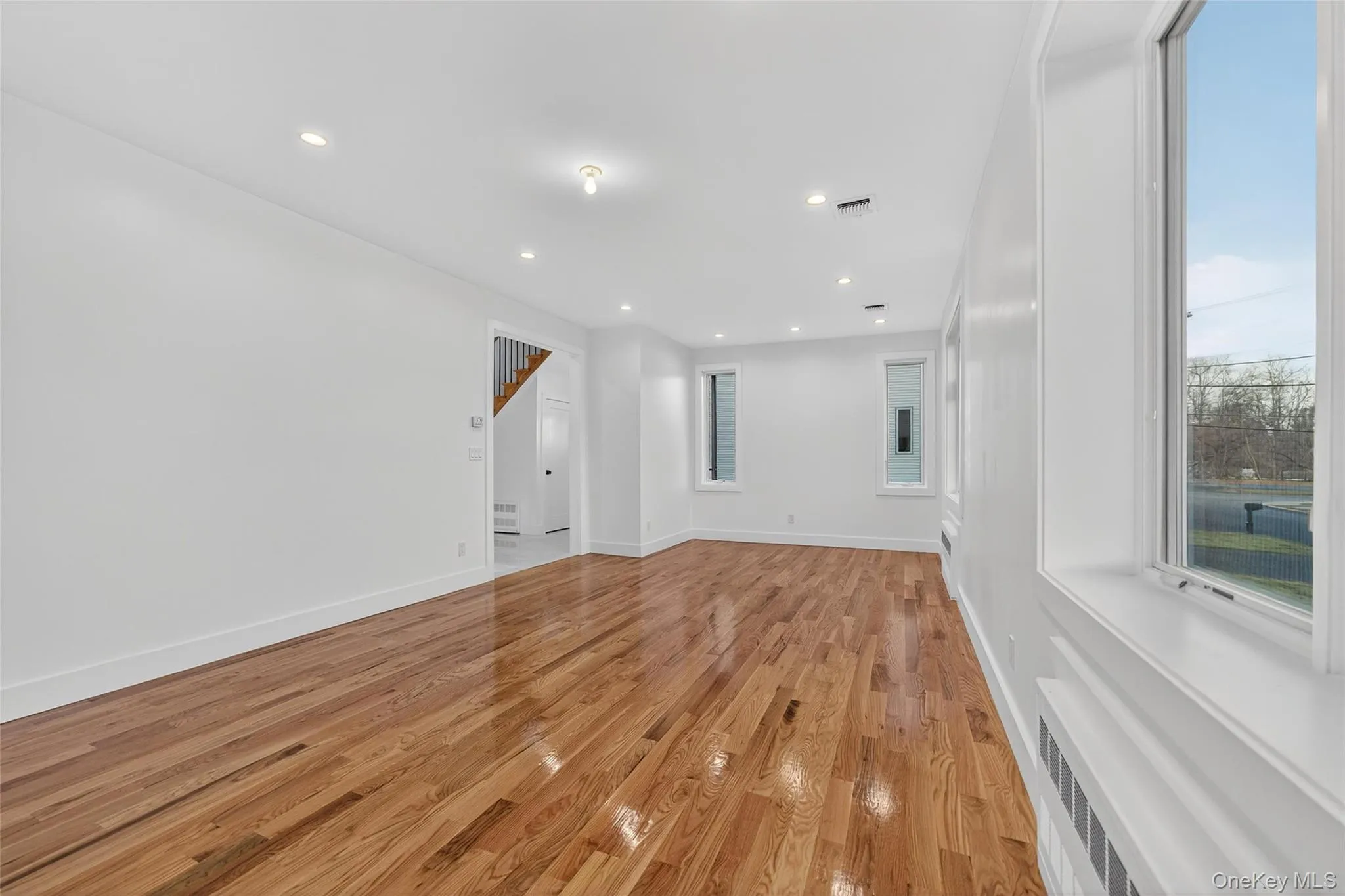 Spare room featuring light wood-style flooring, recessed lighting, radiator heating unit, and stairs Spare room featuring light wood-style flooring, recessed lighting, radiator heating unit, and stairs
