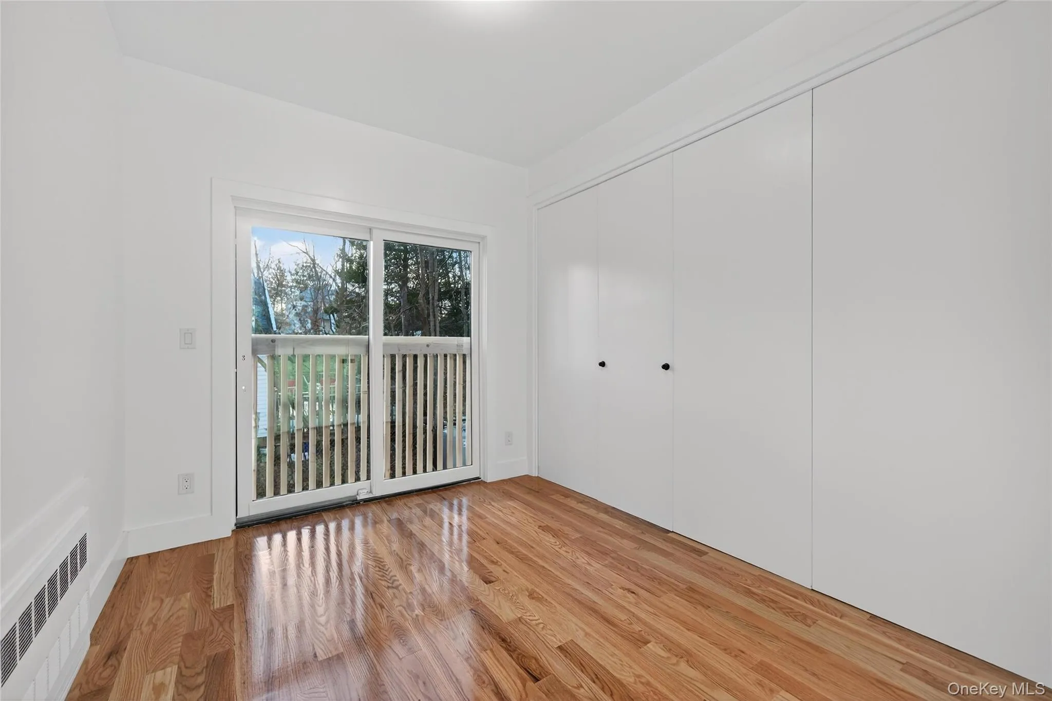 Unfurnished bedroom featuring radiator heating unit, light wood finished floors, a closet, and access to outside Unfurnished bedroom featuring radiator heating unit, light wood finished floors, a closet, and access to outside