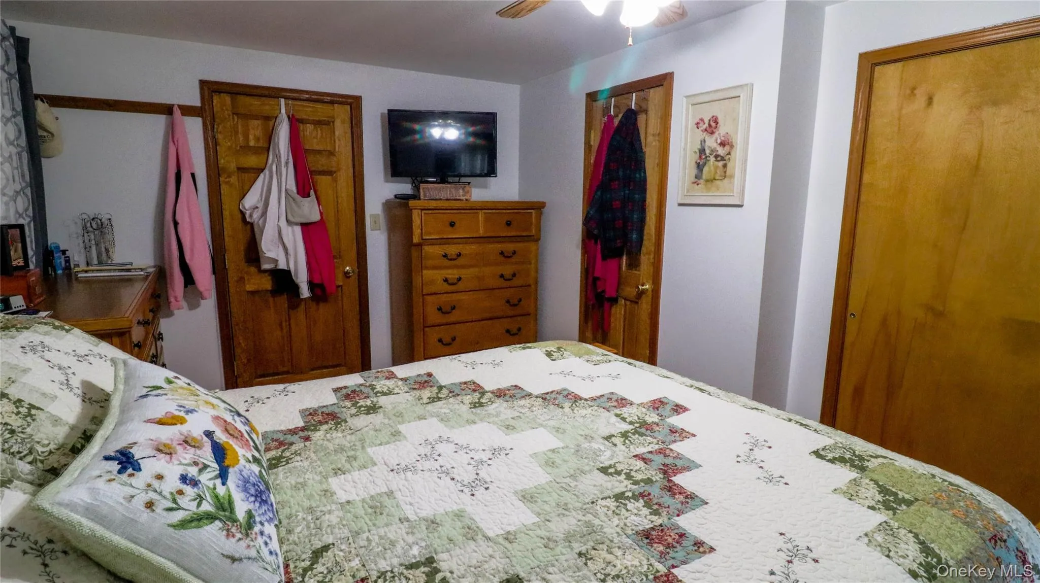 Bedroom featuring multiple wood-paneled doors, wood-finish flooring, and a ceiling fan Bedroom featuring multiple wood-paneled doors, wood-finish flooring, and a ceiling fan