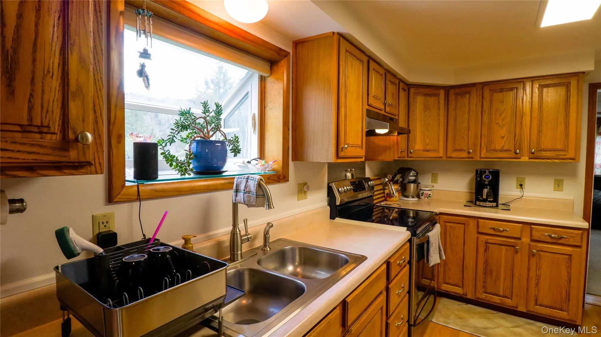 Kitchen featuring wood cabinetry, a double basin stainless steel sink, light-toned countertops, and a black electric range Kitchen featuring wood cabinetry, a double basin stainless steel sink, light-toned countertops, and a black electric range