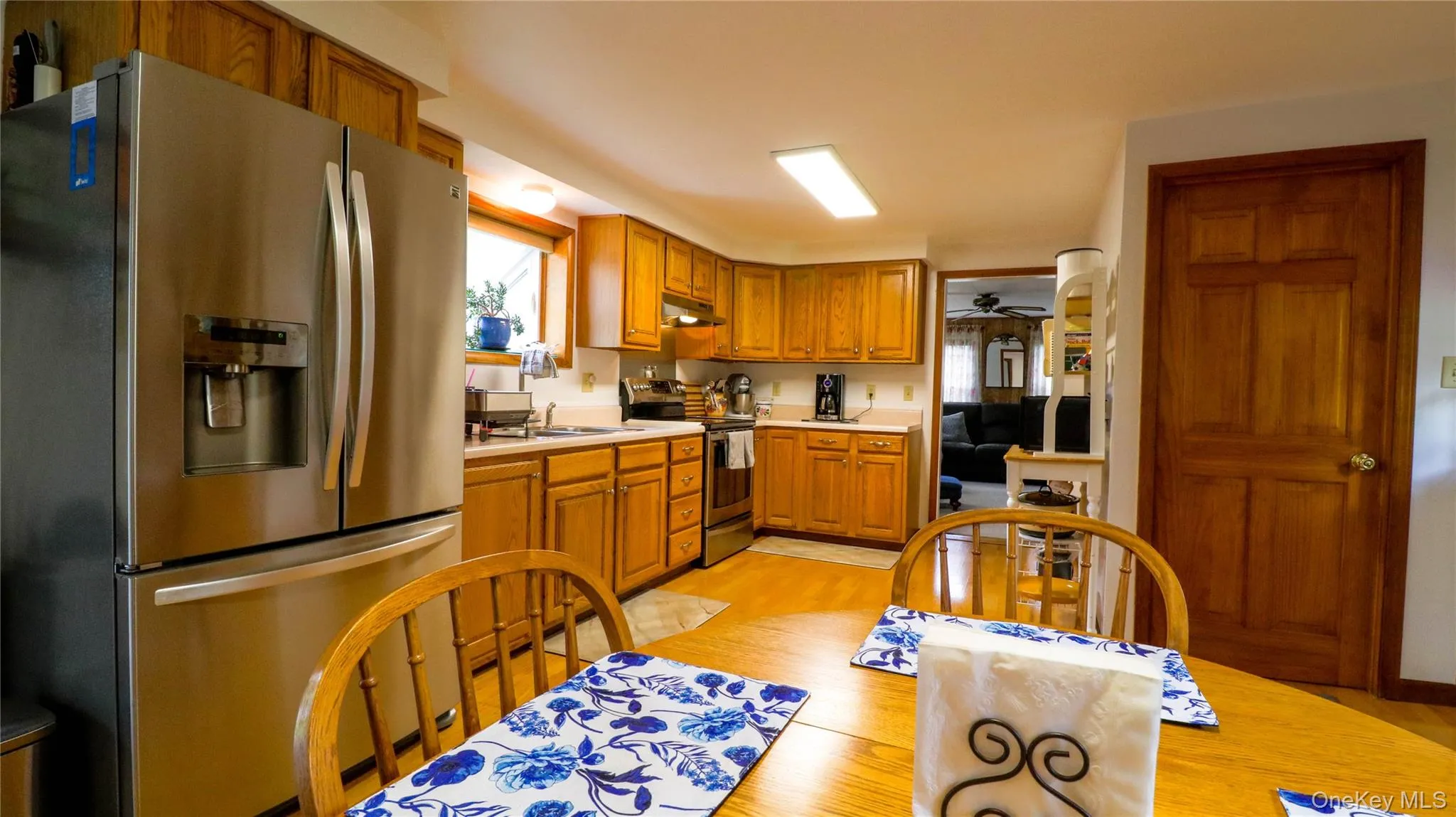 Kitchen featuring wood-finish cabinetry, stainless steel refrigerator, neutral countertops, and wood-finish flooring Kitchen featuring wood-finish cabinetry, stainless steel refrigerator, neutral countertops, and wood-finish flooring