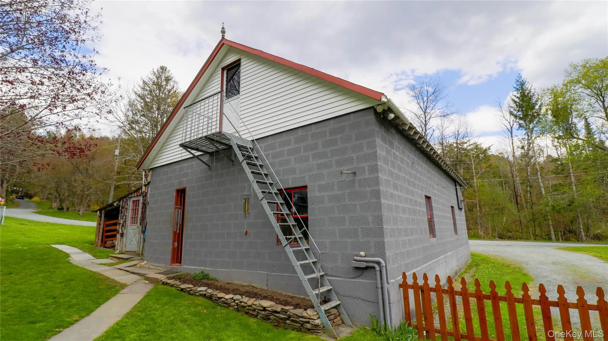 Gray cinder block exterior with a white gable-end facade, red-trimmed roofline, and an external metal staircase leading to a second-story balcony Gray cinder block exterior with a white gable-end facade, red-trimmed roofline, and an external metal staircase leading to a second-story balcony