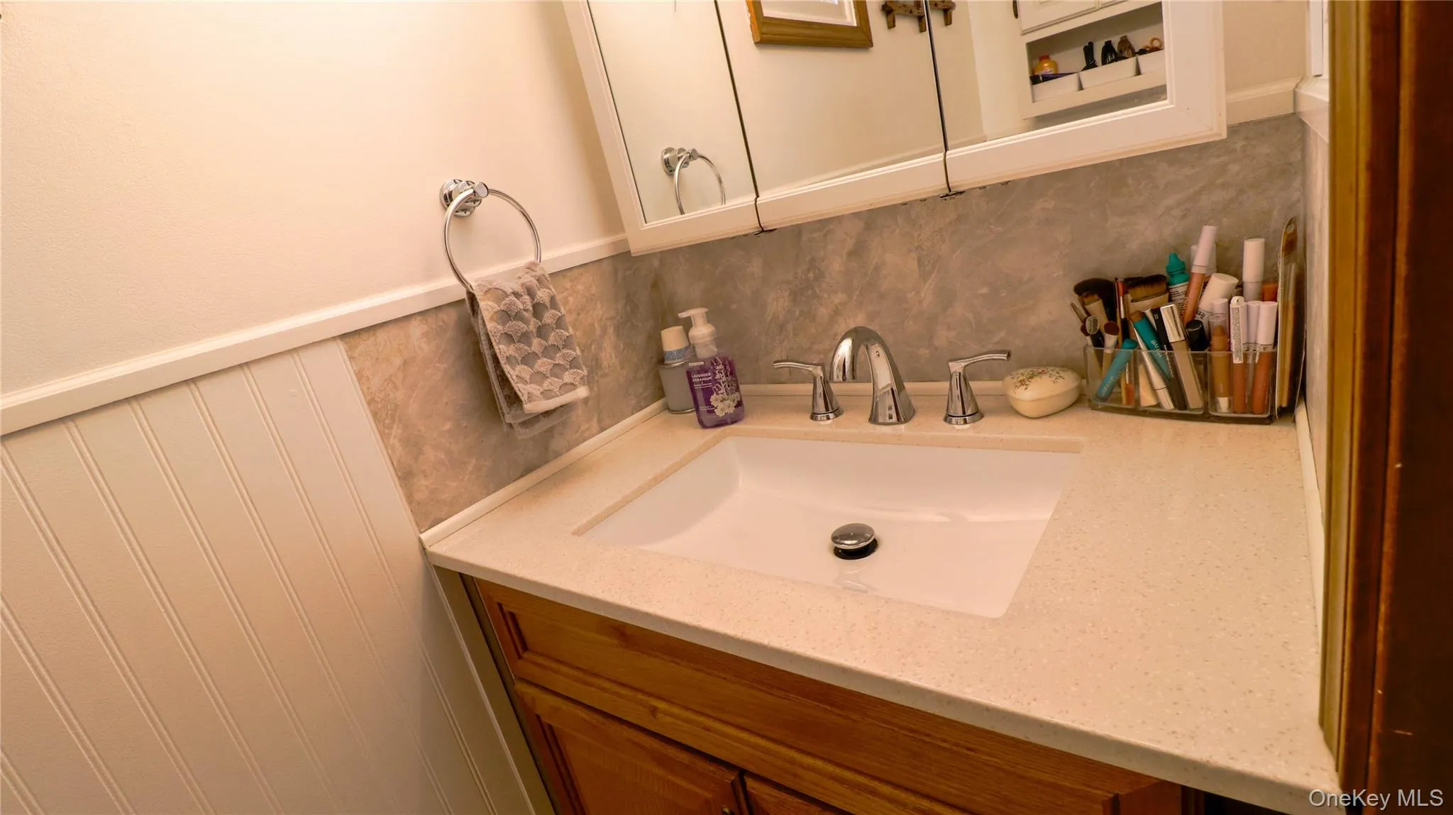 Bathroom vanity featuring a light-colored solid surface countertop with an integrated rectangular sink and chrome faucet Bathroom vanity featuring a light-colored solid surface countertop with an integrated rectangular sink and chrome faucet