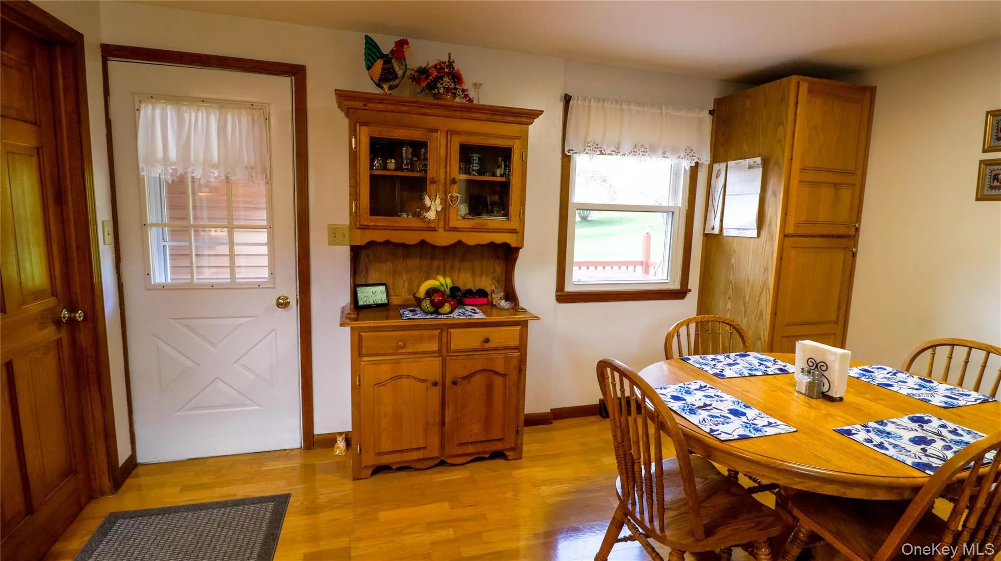 Bright interior featuring wood-finish flooring, a white paneled door with a grid window, and a built-in wood-tone storage cabinet Bright interior featuring wood-finish flooring, a white paneled door with a grid window, and a built-in wood-tone storage cabinet