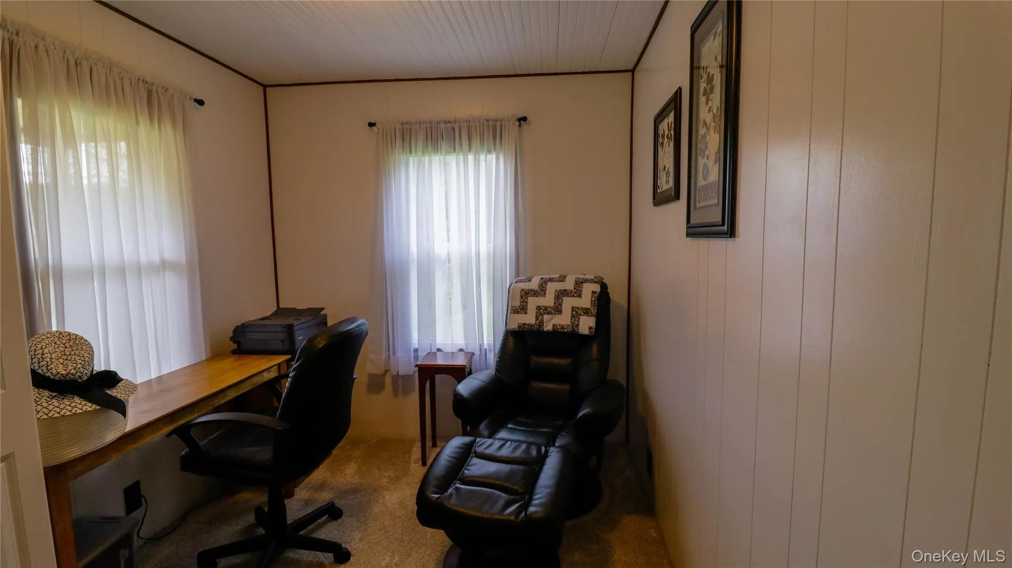 Room featuring two windows with sheer curtains, a built-in wood-finish desk, vertical wall paneling, and a white beadboard ceiling Room featuring two windows with sheer curtains, a built-in wood-finish desk, vertical wall paneling, and a white beadboard ceiling