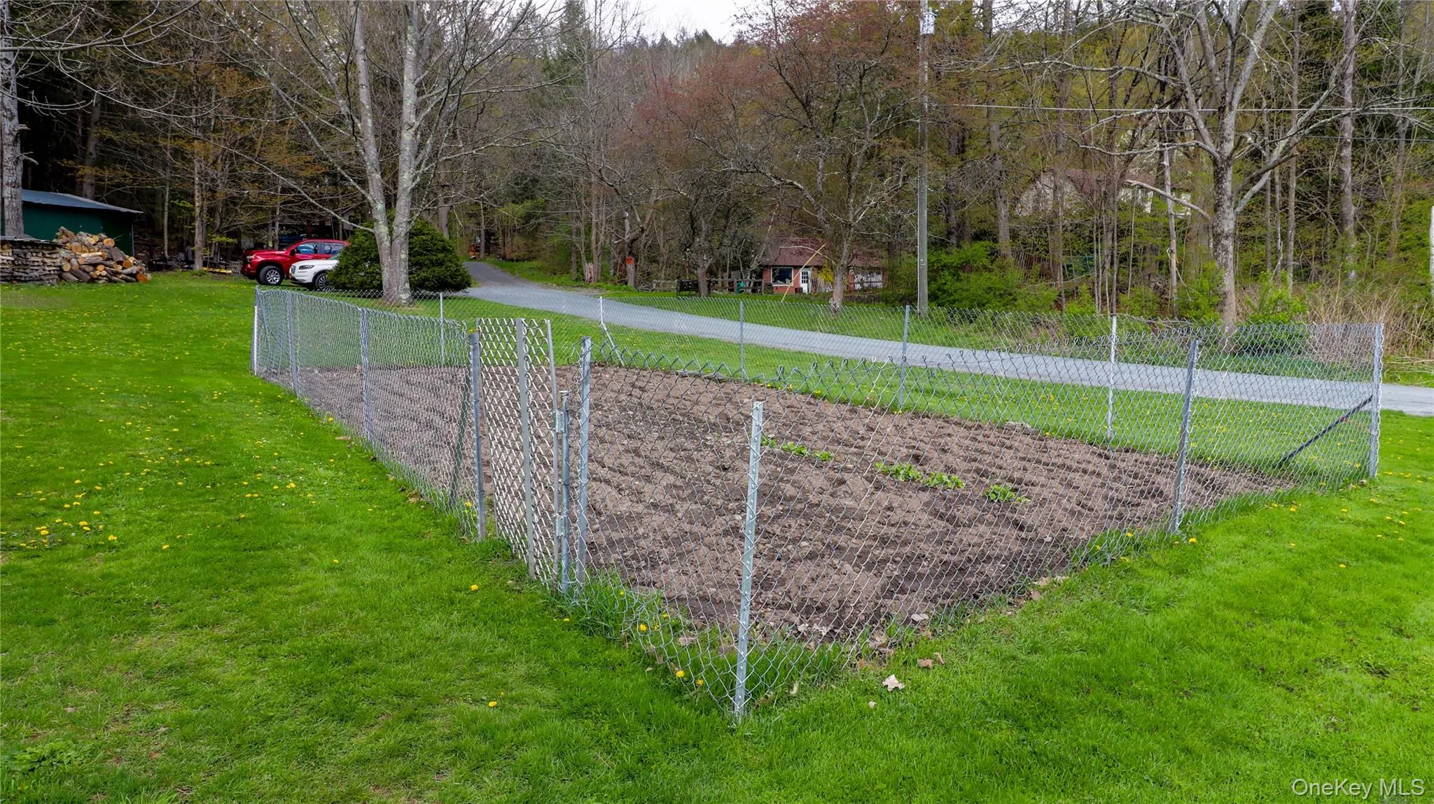 Fenced garden plot with tilled soil, surrounded by a manicured lawn and mature trees Fenced garden plot with tilled soil, surrounded by a manicured lawn and mature trees