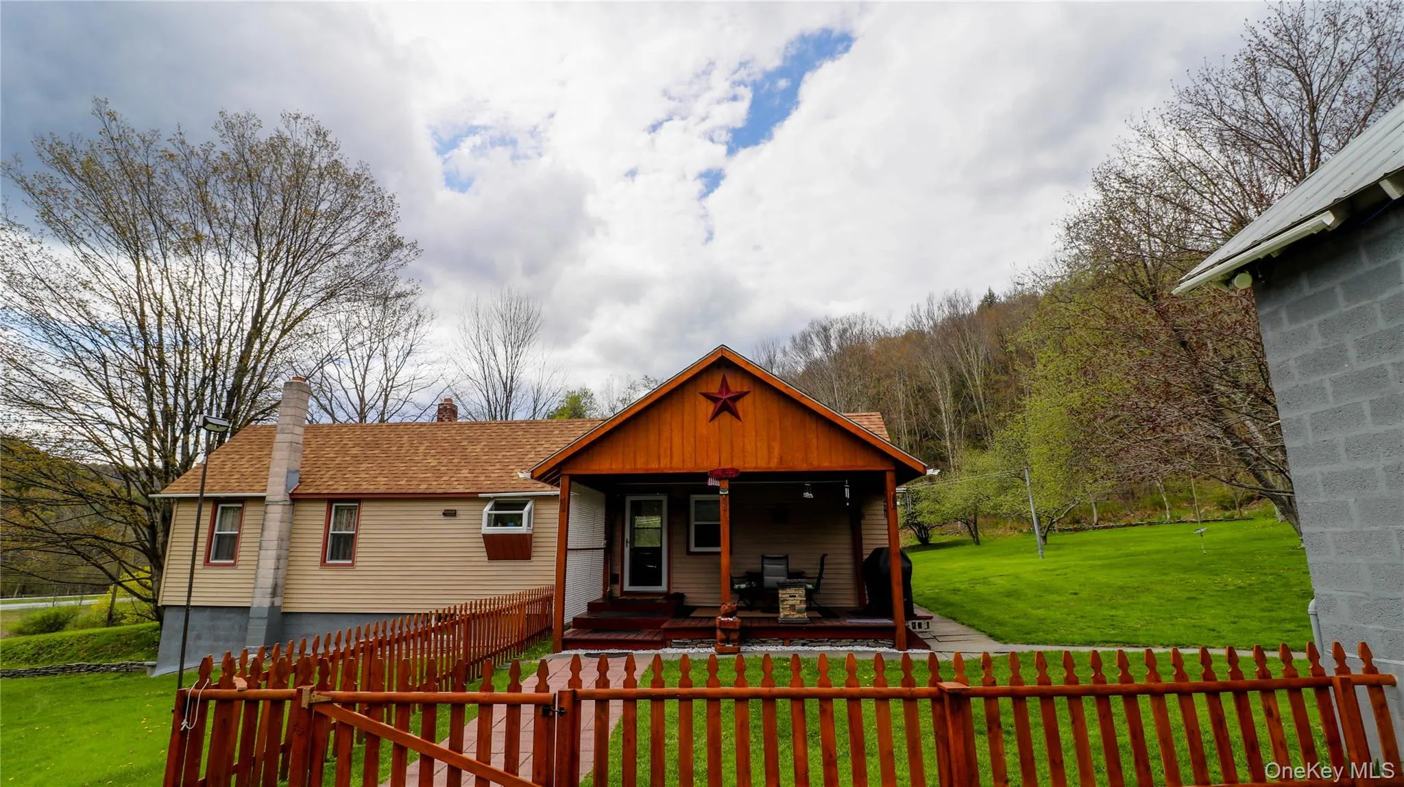 Ranch-style residence featuring a prominent covered front porch with exposed wood beams, a red star decorative element, and a wooden deck Ranch-style residence featuring a prominent covered front porch with exposed wood beams, a red star decorative element, and a wooden deck
