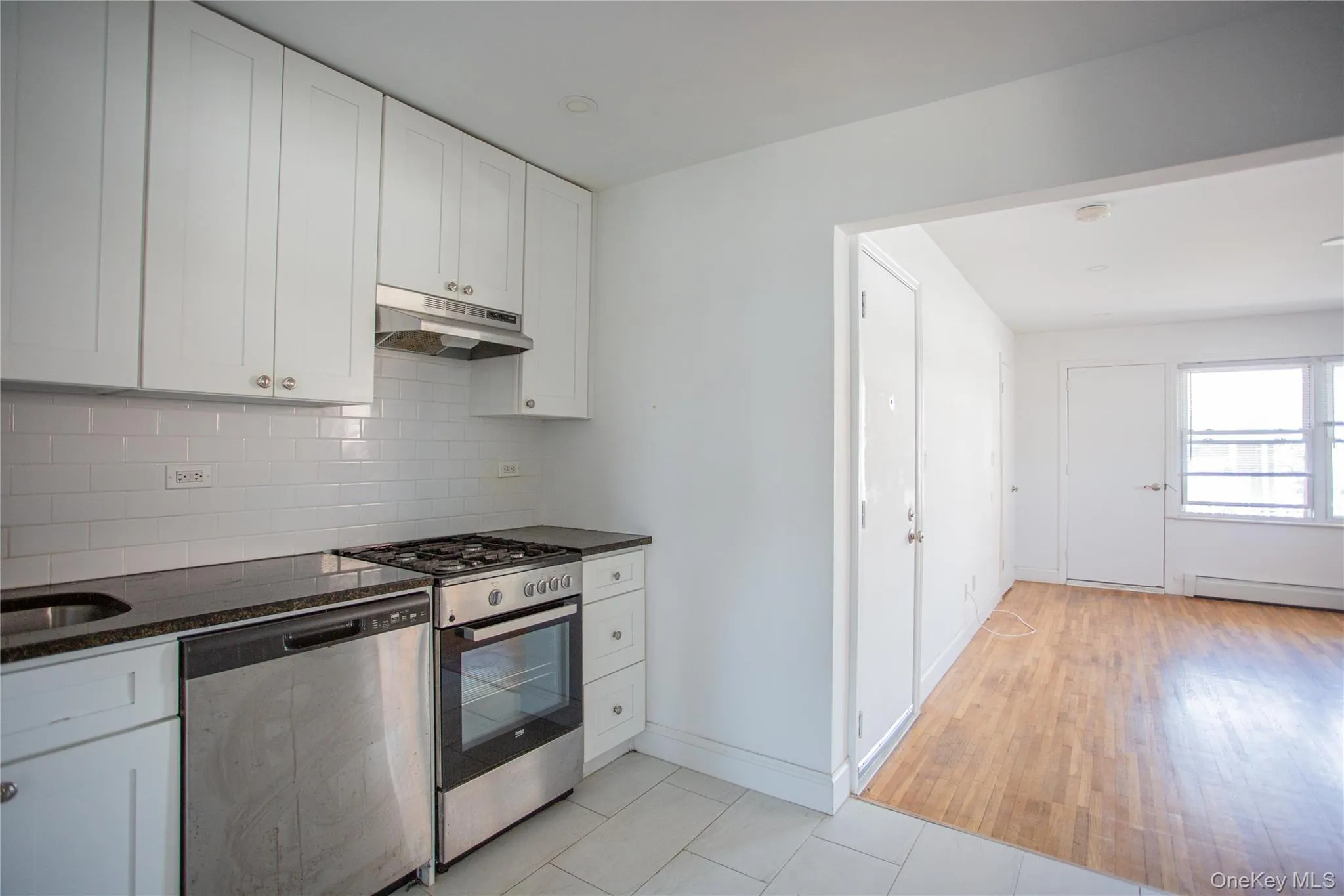 Kitchen featuring white cabinets, appliances with stainless steel finishes, backsplash, under cabinet range hood, and dark stone counters Kitchen featuring white cabinets, appliances with stainless steel finishes, backsplash, under cabinet range hood, and dark stone counters