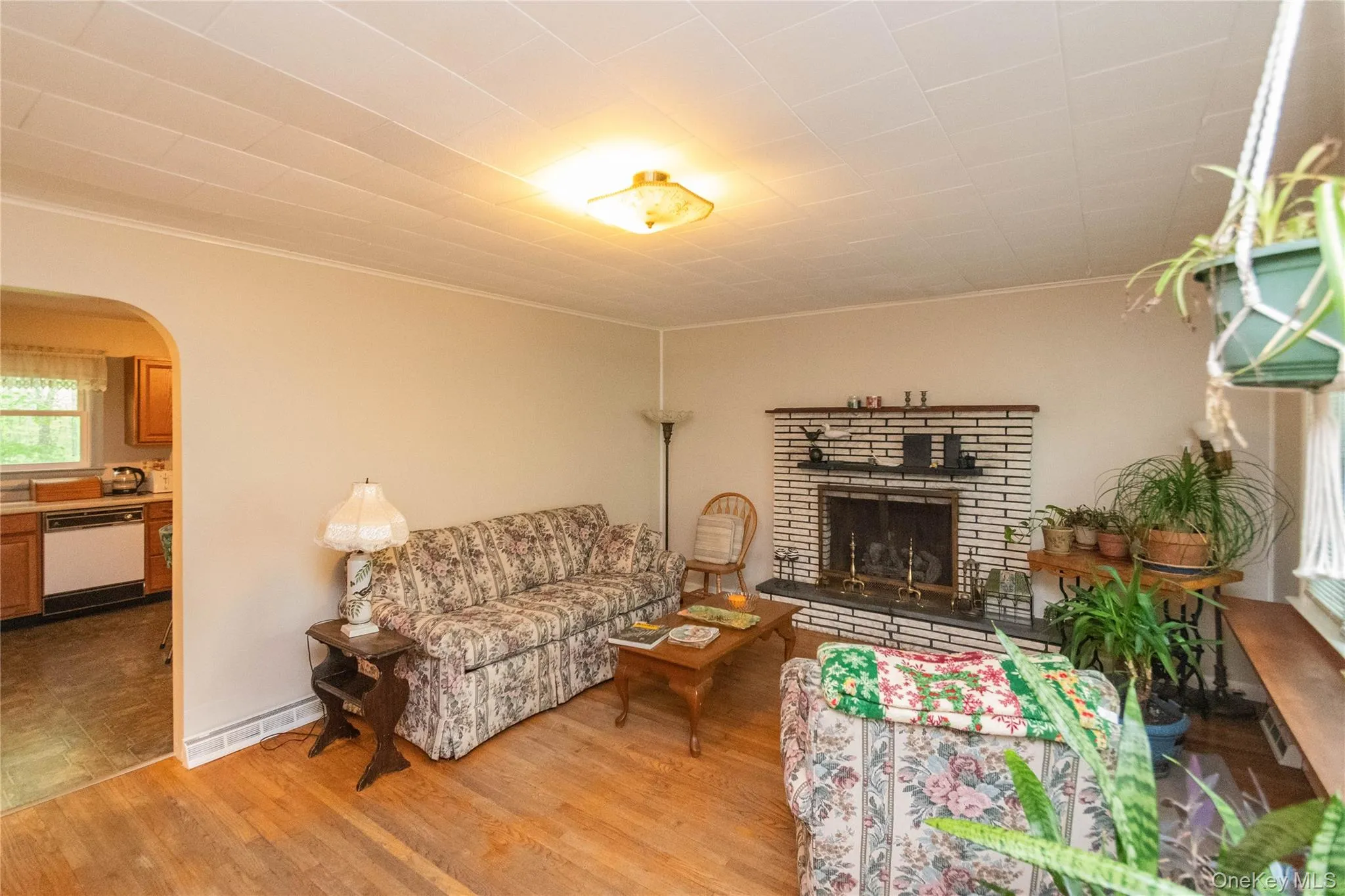 Living area featuring wood-finish flooring, a white brick fireplace with a black hearth, and an arched doorway Living area featuring wood-finish flooring, a white brick fireplace with a black hearth, and an arched doorway