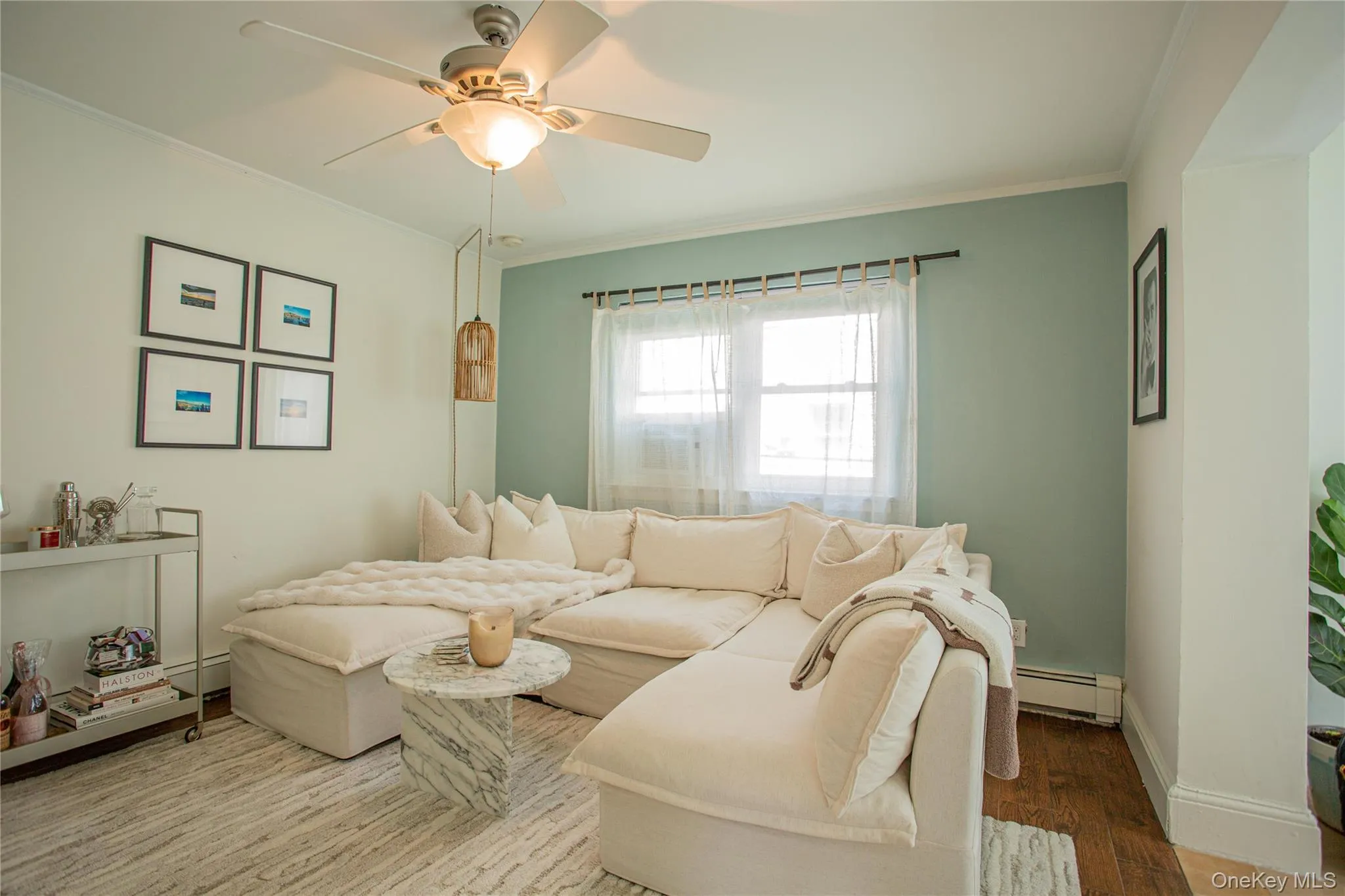 Living area featuring a baseboard heating unit, wood finished floors, a ceiling fan, ornamental molding, and baseboards Living area featuring a baseboard heating unit, wood finished floors, a ceiling fan, ornamental molding, and baseboards