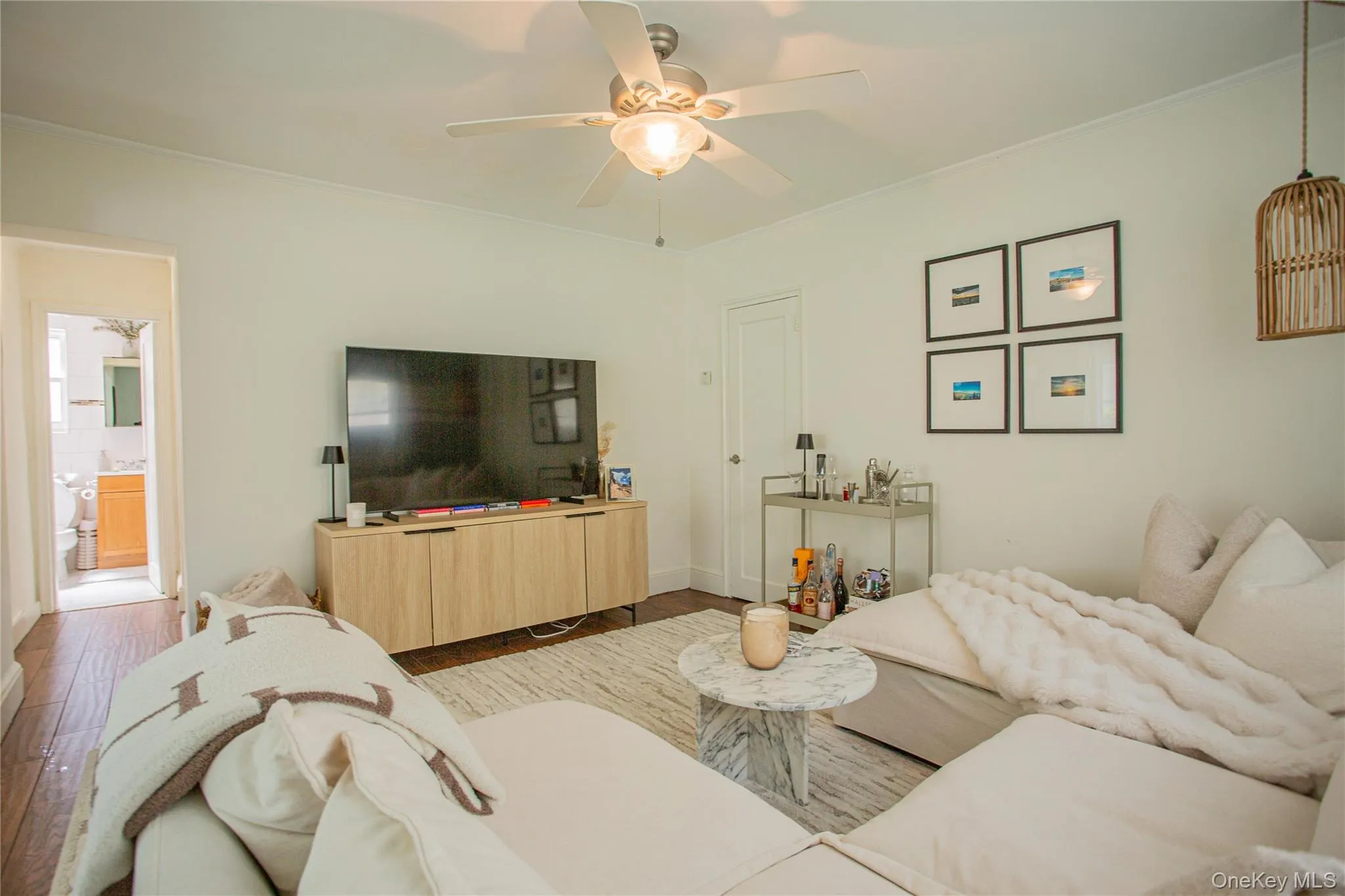 Living room featuring wood finished floors, a ceiling fan, crown molding, and baseboards Living room featuring wood finished floors, a ceiling fan, crown molding, and baseboards