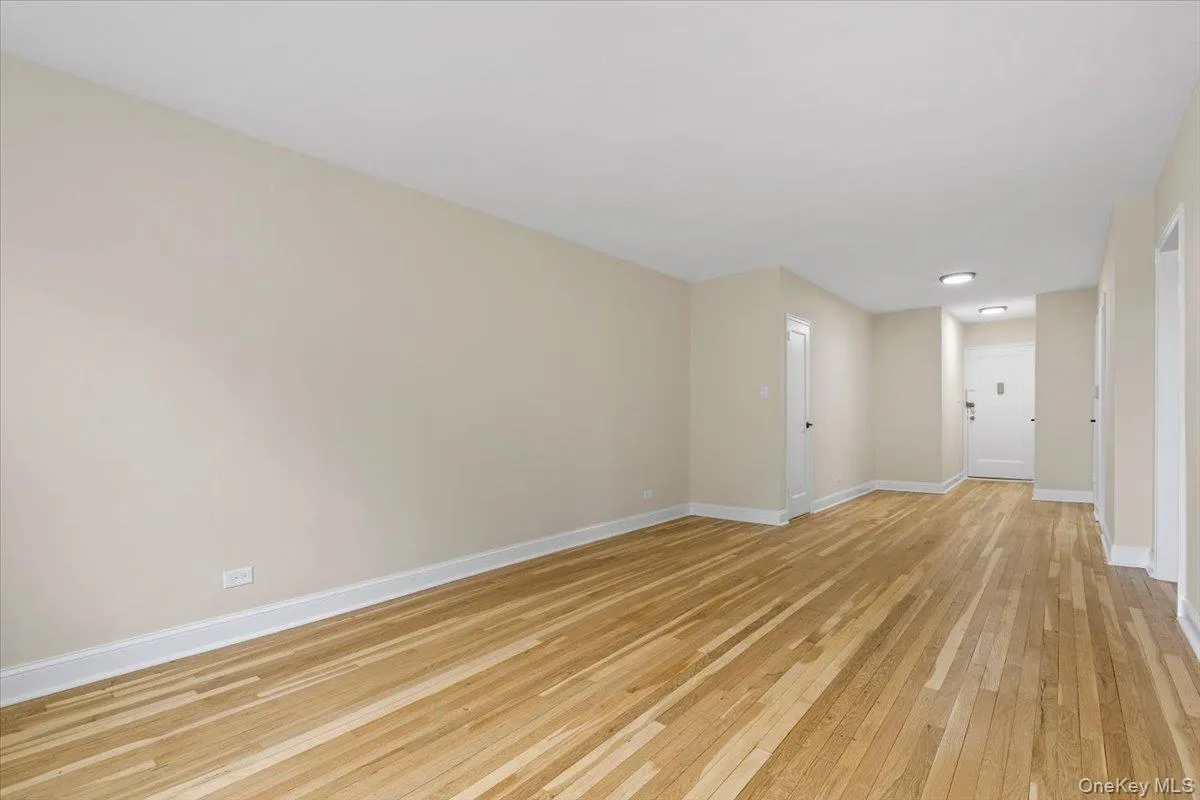Spacious living room featuring wood-finish flooring, light-toned walls, and white baseboards Spacious living room featuring wood-finish flooring, light-toned walls, and white baseboards
