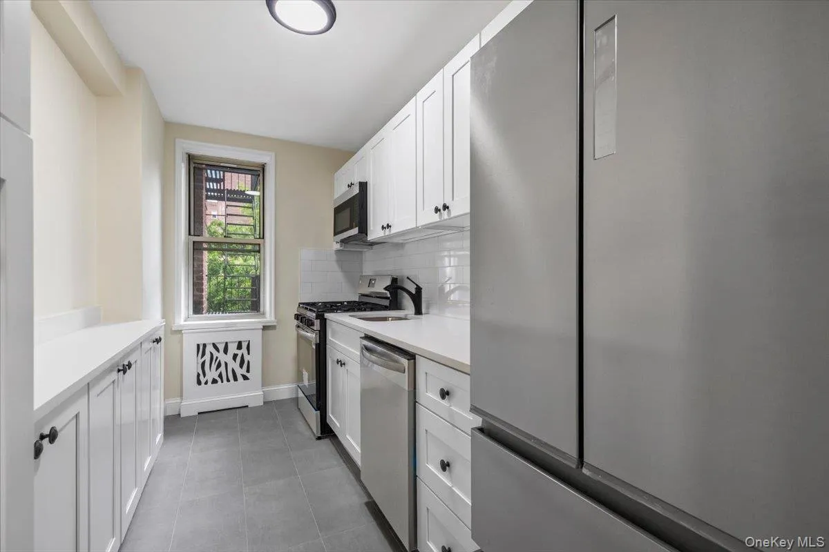 Modern kitchen featuring stainless steel appliances, white shaker-style cabinetry, light countertops, and a subway tile backsplash Modern kitchen featuring stainless steel appliances, white shaker-style cabinetry, light countertops, and a subway tile backsplash