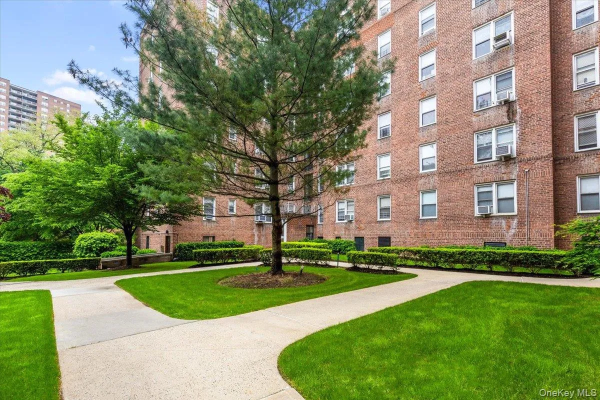Brick exterior building featuring multiple windows and a tree-lined landscaped courtyard with paved walkways Brick exterior building featuring multiple windows and a tree-lined landscaped courtyard with paved walkways