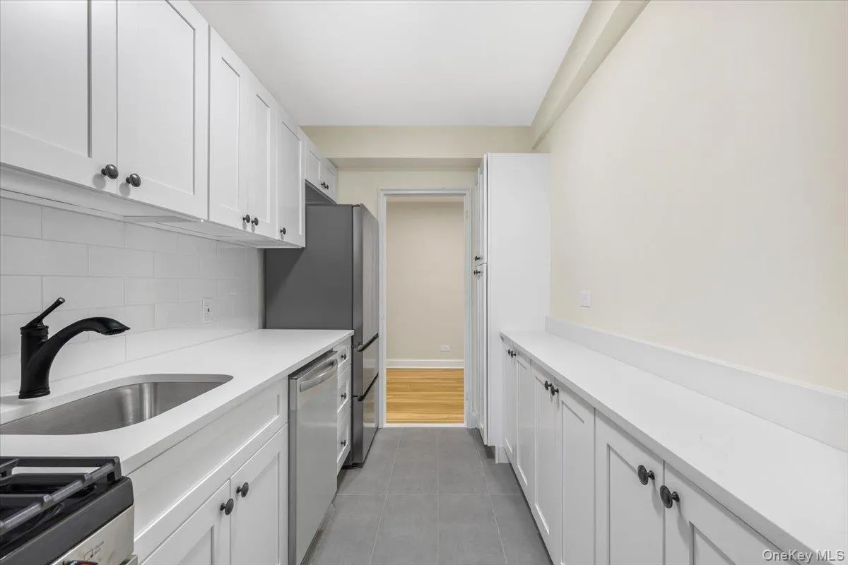 Galley kitchen featuring white shaker-style cabinetry, white subway tile backsplash, stainless steel appliances, and a matte black faucet Galley kitchen featuring white shaker-style cabinetry, white subway tile backsplash, stainless steel appliances, and a matte black faucet