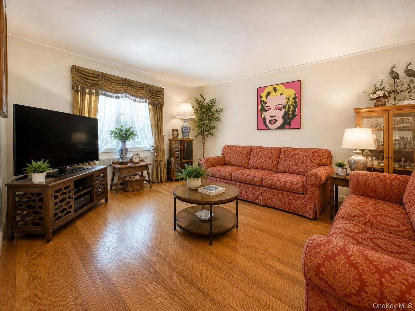 Hardwood flooring enhances this living space, featuring a window with decorative valance and curtains Hardwood flooring enhances this living space, featuring a window with decorative valance and curtains