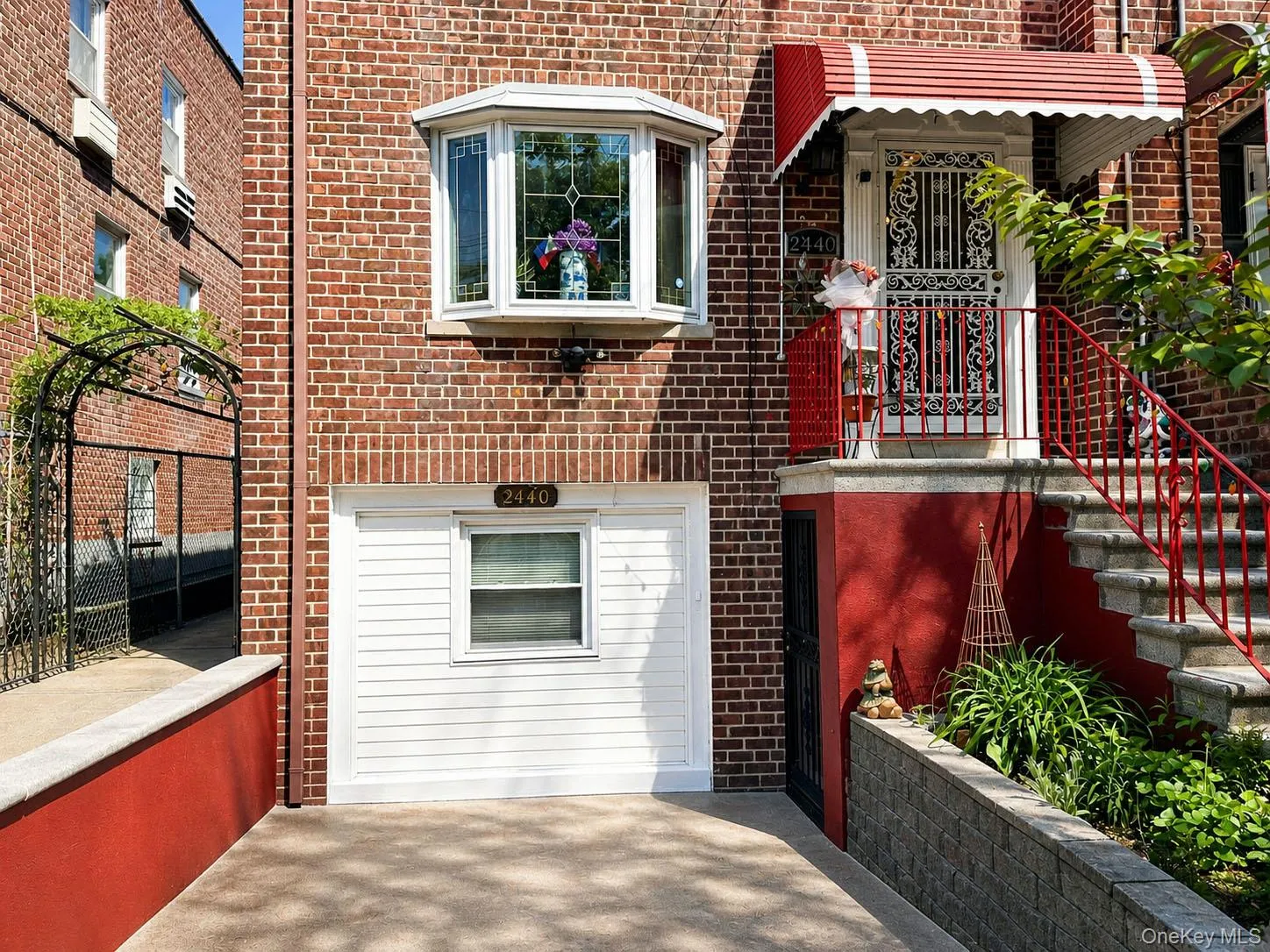 Brick facade residence featuring a street-level garage, a prominent bay window with decorative glass, and a main entry with a striped awning Brick facade residence featuring a street-level garage, a prominent bay window with decorative glass, and a main entry with a striped awning