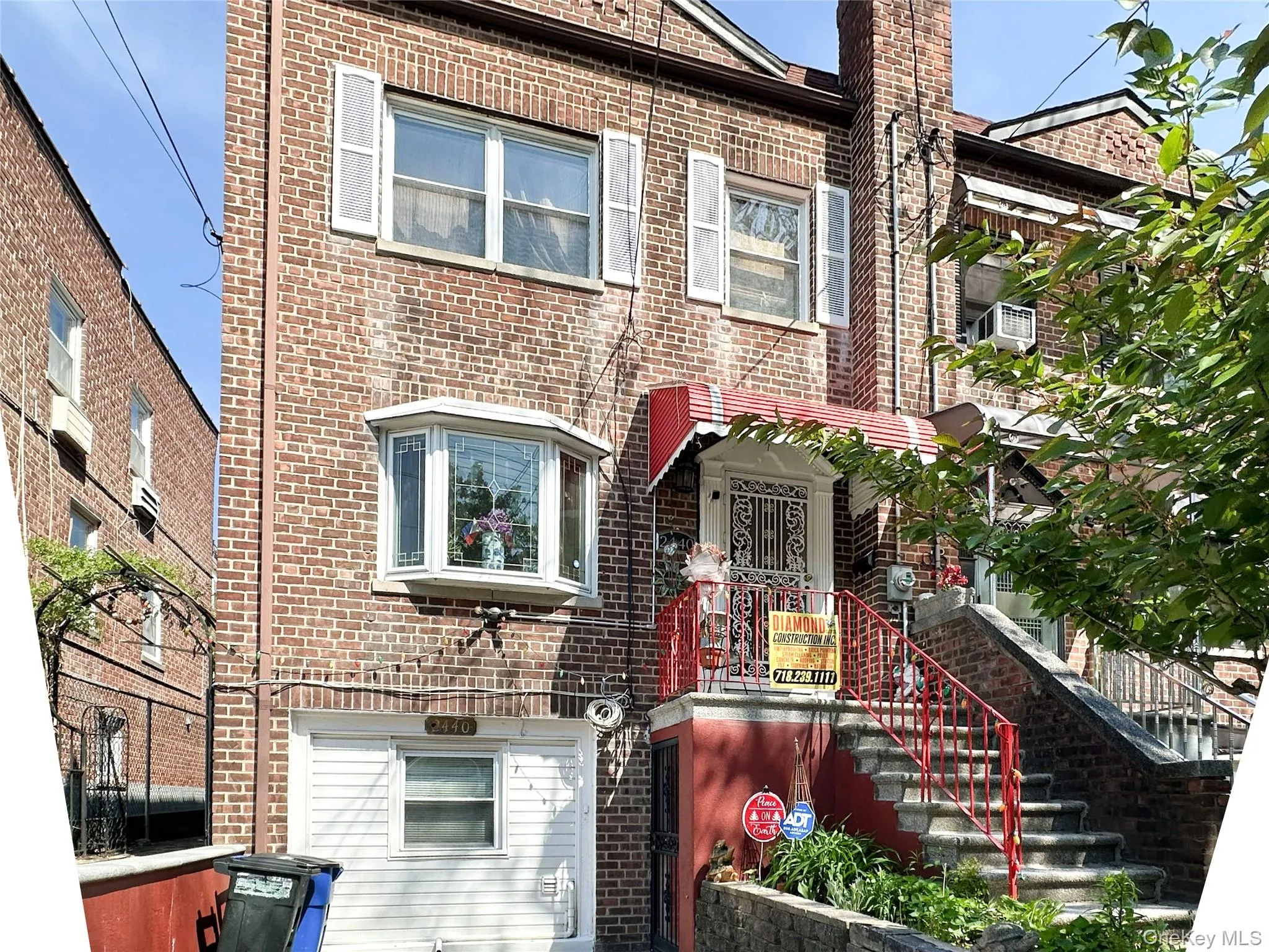 Brick facade residence featuring a prominent bay window, upper-level windows with shutters, a covered entryway with a security door, and a red-railed exterior staircase Brick facade residence featuring a prominent bay window, upper-level windows with shutters, a covered entryway with a security door, and a red-railed exterior staircase