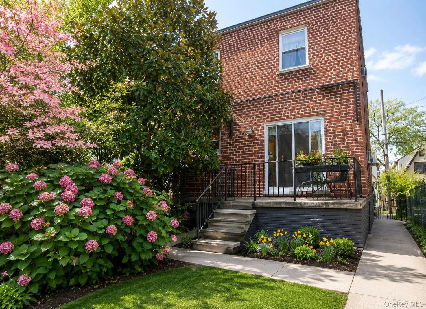 Brick exterior featuring a private patio, sliding glass door access, exterior stairs, and vibrant landscaping with pink hydrangeas and flowering trees Brick exterior featuring a private patio, sliding glass door access, exterior stairs, and vibrant landscaping with pink hydrangeas and flowering trees