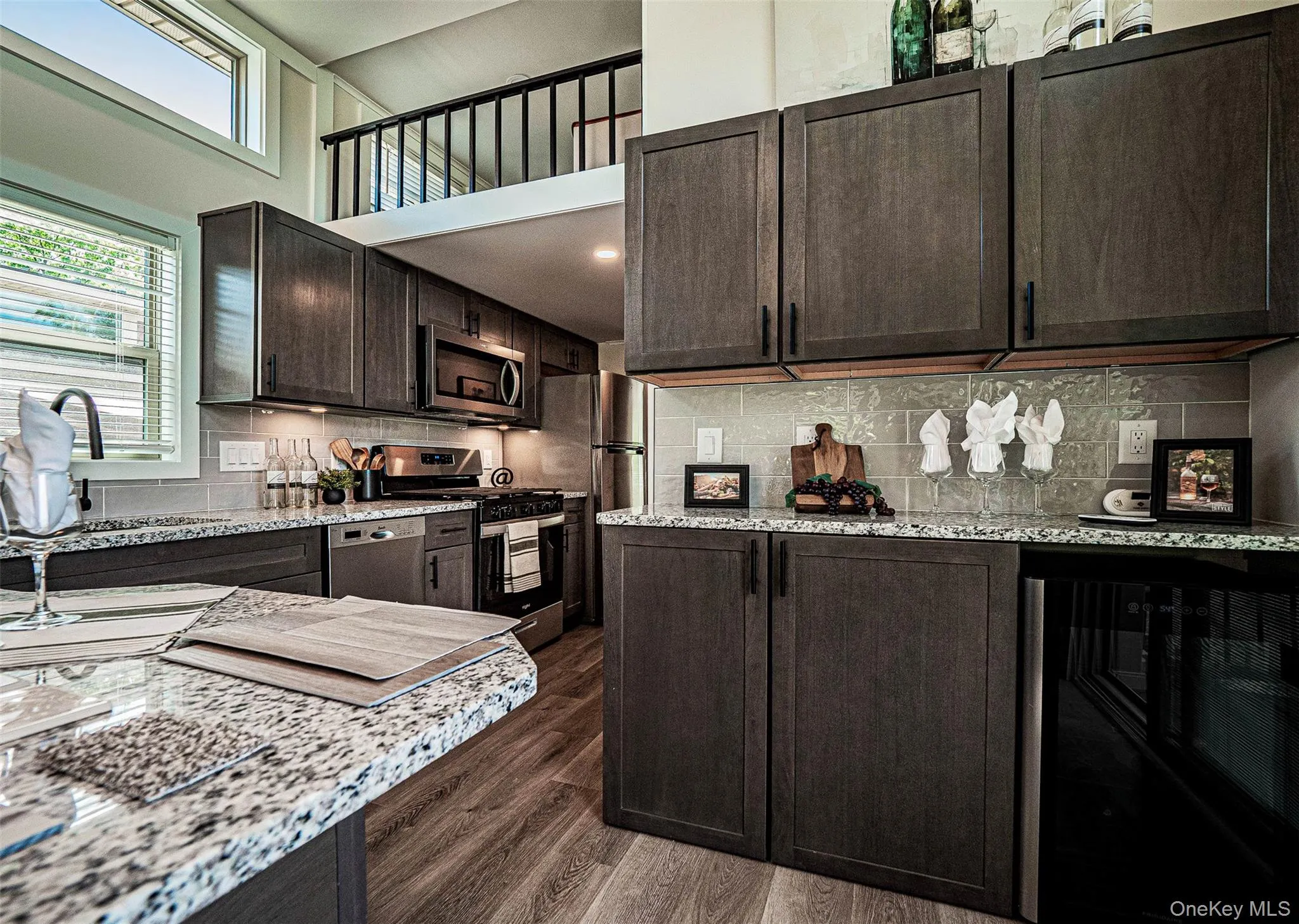Kitchen featuring appliances with stainless steel finishes, light stone counters, dark brown cabinetry, and a towering ceiling Kitchen featuring appliances with stainless steel finishes, light stone counters, dark brown cabinetry, and a towering ceiling