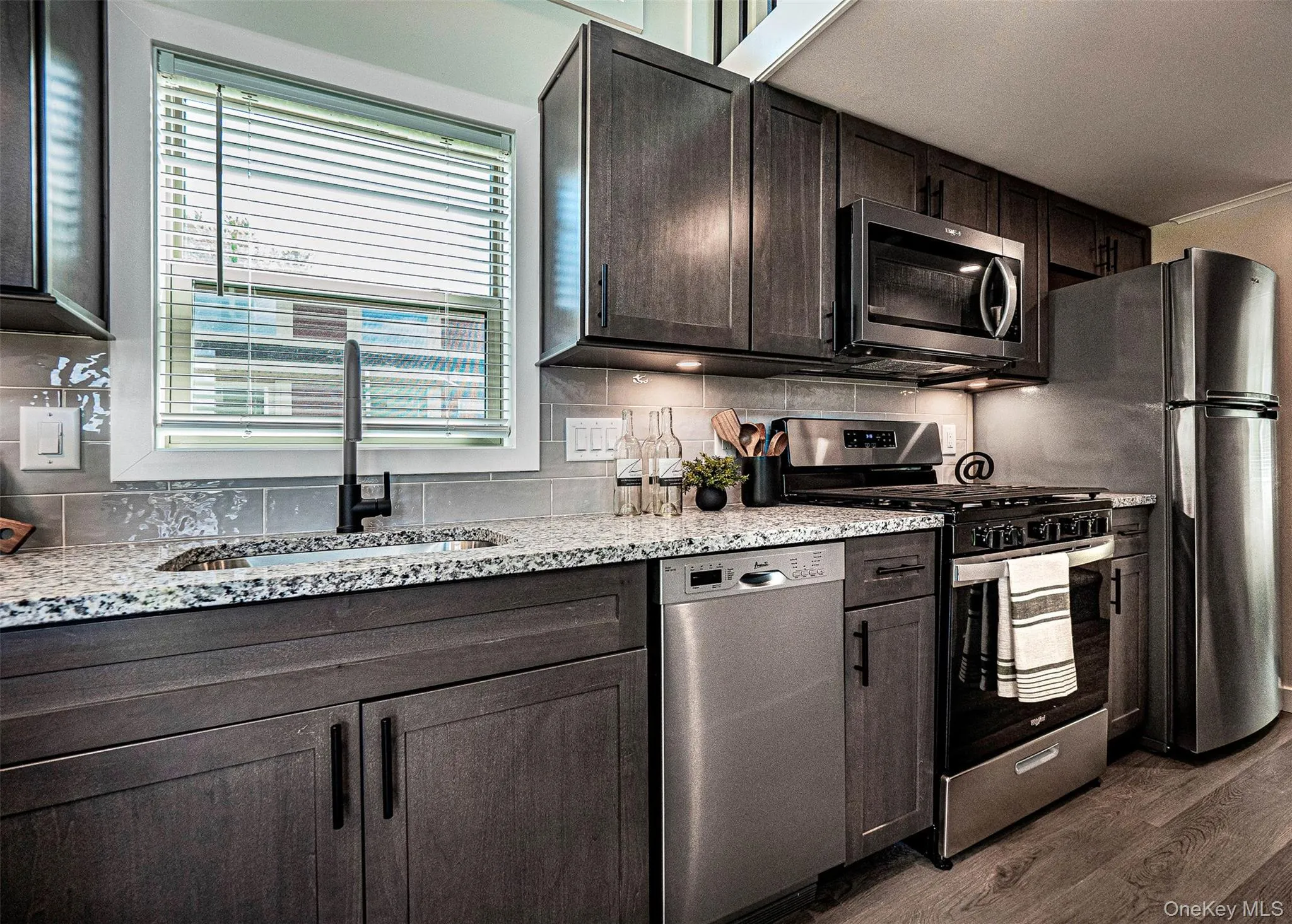 Kitchen featuring appliances with stainless steel finishes, light stone countertops, tasteful backsplash, and dark brown cabinetry Kitchen featuring appliances with stainless steel finishes, light stone countertops, tasteful backsplash, and dark brown cabinetry