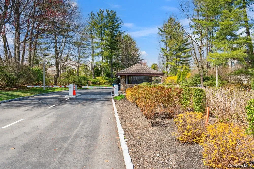 Entry gate with security arm, featuring a stone and wood gatehouse, surrounded by mature trees and landscaped shrubbery Entry gate with security arm, featuring a stone and wood gatehouse, surrounded by mature trees and landscaped shrubbery