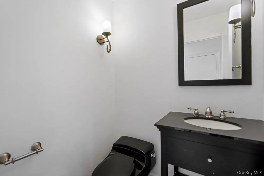 Bathroom featuring a black toilet, dark vanity with an integrated sink, brushed nickel faucet, framed mirror, and a wall-mounted sconce Bathroom featuring a black toilet, dark vanity with an integrated sink, brushed nickel faucet, framed mirror, and a wall-mounted sconce
