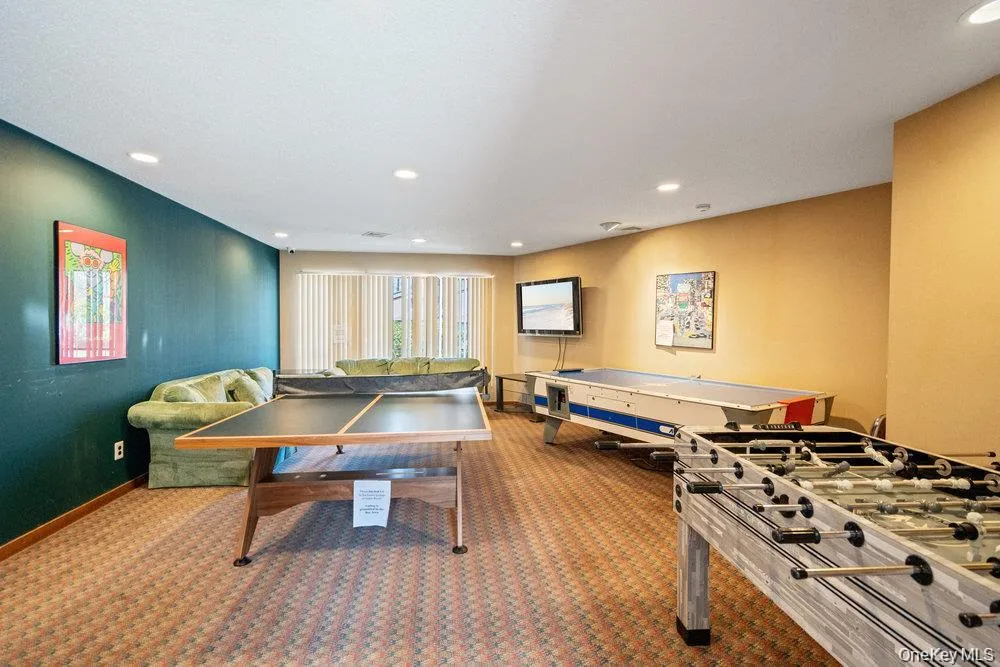 Recreation room featuring recessed lighting, patterned carpet flooring, and a window with vertical blinds Recreation room featuring recessed lighting, patterned carpet flooring, and a window with vertical blinds