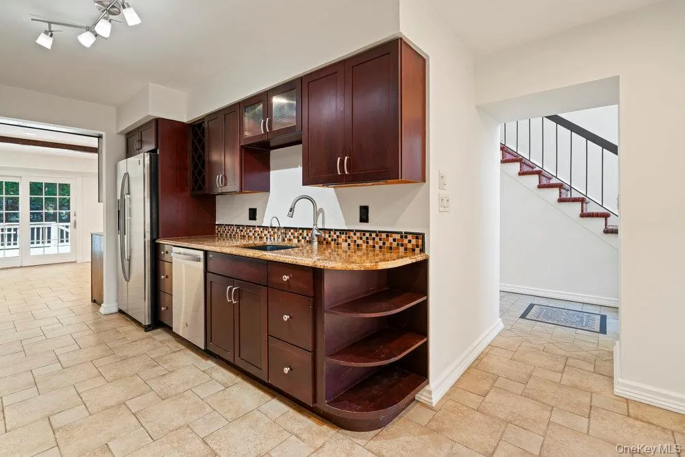 Kitchenette featuring dark wood cabinetry, stainless steel appliances, granite-style countertops, mosaic tile backsplash, and tile flooring Kitchenette featuring dark wood cabinetry, stainless steel appliances, granite-style countertops, mosaic tile backsplash, and tile flooring