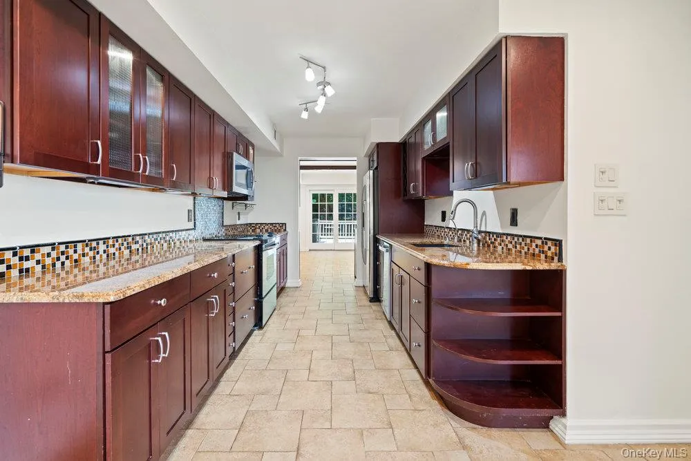 Galley-style kitchen featuring dark wood cabinetry, granite-finish countertops, and a mosaic tile backsplash Galley-style kitchen featuring dark wood cabinetry, granite-finish countertops, and a mosaic tile backsplash