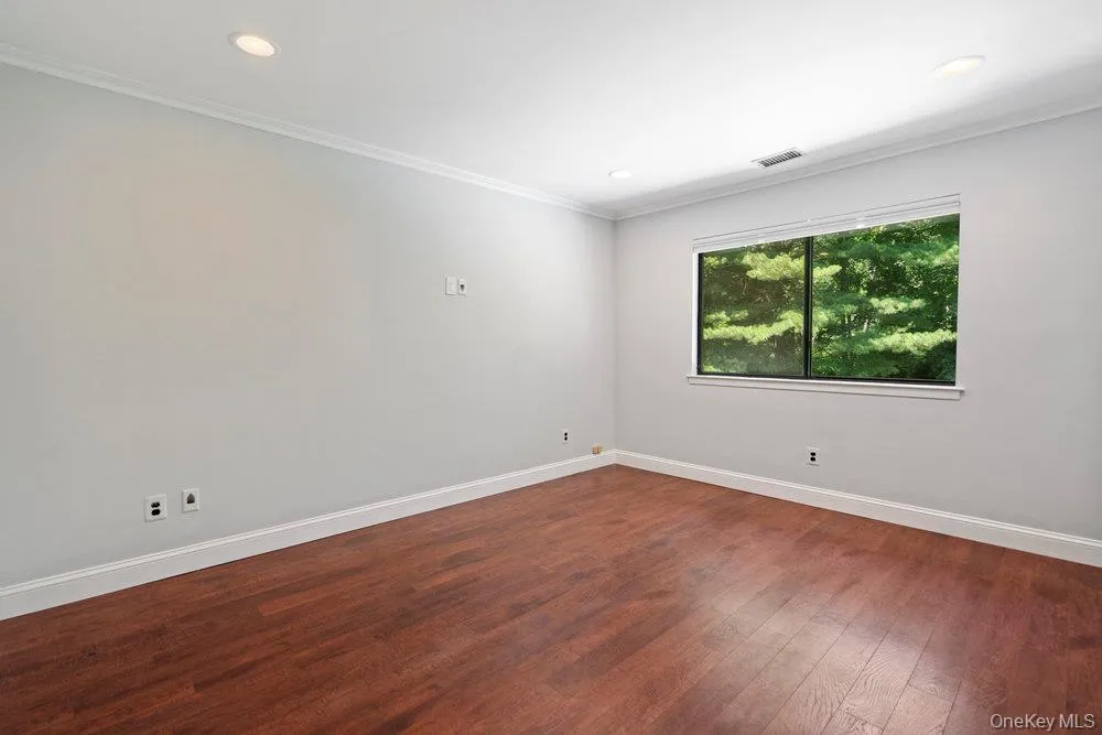 Spacious room featuring wood-finish flooring, white baseboards, crown molding, and recessed lighting Spacious room featuring wood-finish flooring, white baseboards, crown molding, and recessed lighting