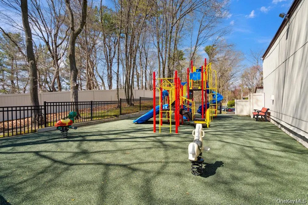 Outdoor playground featuring a multi-level play structure with slides and climbing elements, a rubberized safety surface, spring riders, and perimeter fencing Outdoor playground featuring a multi-level play structure with slides and climbing elements, a rubberized safety surface, spring riders, and perimeter fencing