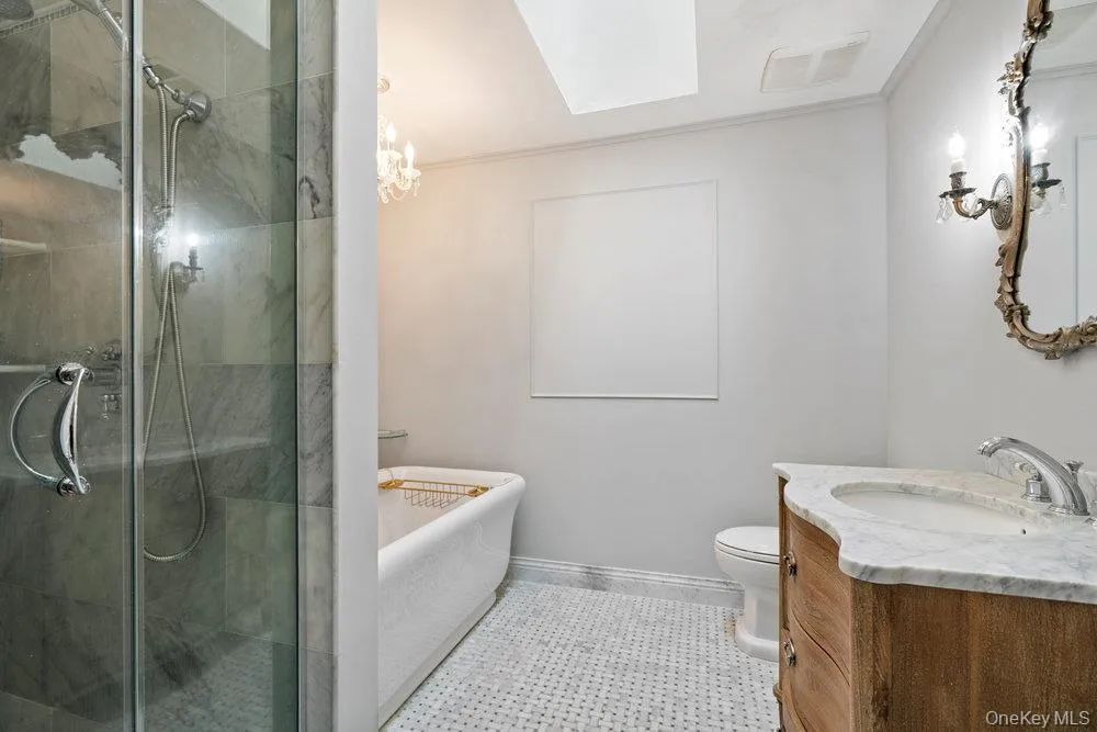 Bathroom featuring a walk-in shower with glass enclosure, freestanding soaking tub, wood-finish vanity with marble countertop, and a decorative wall mirror with sconce lighting Bathroom featuring a walk-in shower with glass enclosure, freestanding soaking tub, wood-finish vanity with marble countertop, and a decorative wall mirror with sconce lighting