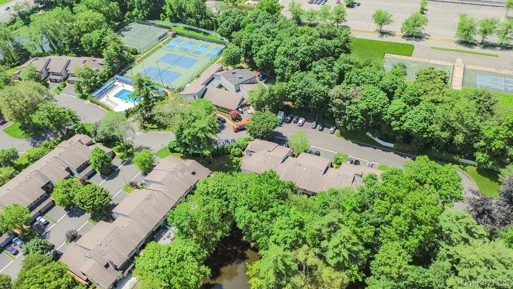 Aerial perspective showcasing multiple residential buildings, surrounded by mature trees, and featuring on-site amenities including a swimming pool and tennis courts Aerial perspective showcasing multiple residential buildings, surrounded by mature trees, and featuring on-site amenities including a swimming pool and tennis courts